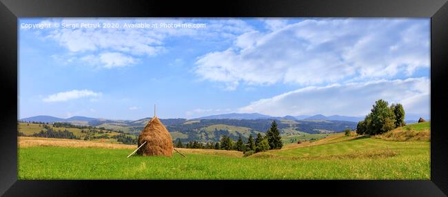 A haystack stands in a meadow against the backdrop of the Carpathian mountains and slopes. Framed Print by Sergii Petruk