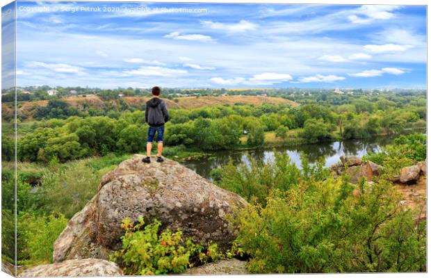 A teenager stands on top of a large stone boulder on the banks of the Southern Bug and looks into the distance. Canvas Print by Sergii Petruk