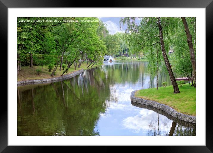 Decorative pond and floating duck house with a fountain in a beautiful picturesque summer park. Framed Mounted Print by Sergii Petruk