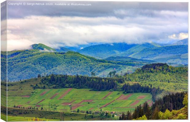 In the valley on the mountainside stretched rectangular agricultural land plots against the backdrop of the picturesque landscape of the Carpathian Mountains, shrouded in mist. Canvas Print by Sergii Petruk