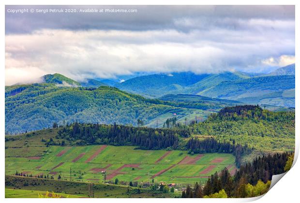 In the valley on the mountainside stretched rectangular agricultural land plots against the backdrop of the picturesque landscape of the Carpathian Mountains, shrouded in mist. Print by Sergii Petruk