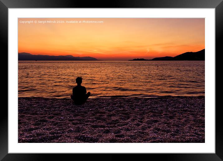 Silhouette of a teenager sitting on the seashore and watching a beautiful, bright sunset on the Gulf of Corinth. Framed Mounted Print by Sergii Petruk