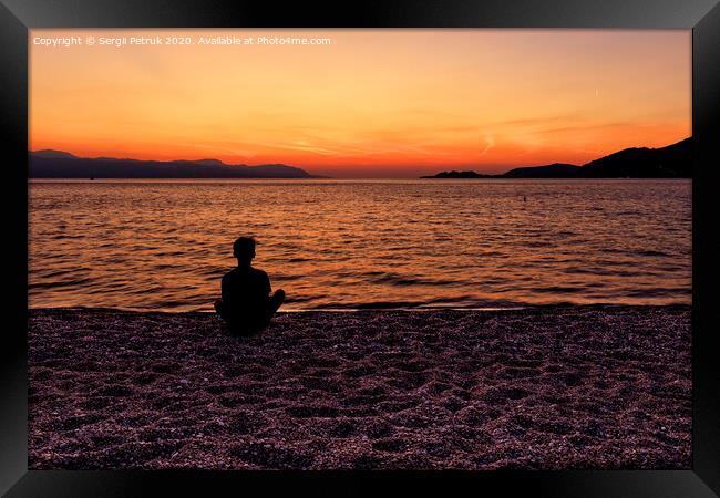 Silhouette of a teenager sitting on the seashore and watching a beautiful, bright sunset on the Gulf of Corinth. Framed Print by Sergii Petruk