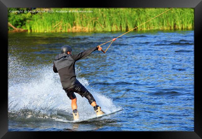 A wakeboarder rushes through the water at high speed along the green bank of the river. Framed Print by Sergii Petruk