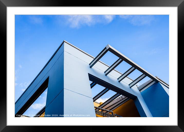 Roof of a blue painted straight design building behind a clear and clear sky at sunset. Framed Mounted Print by Joaquin Corbalan