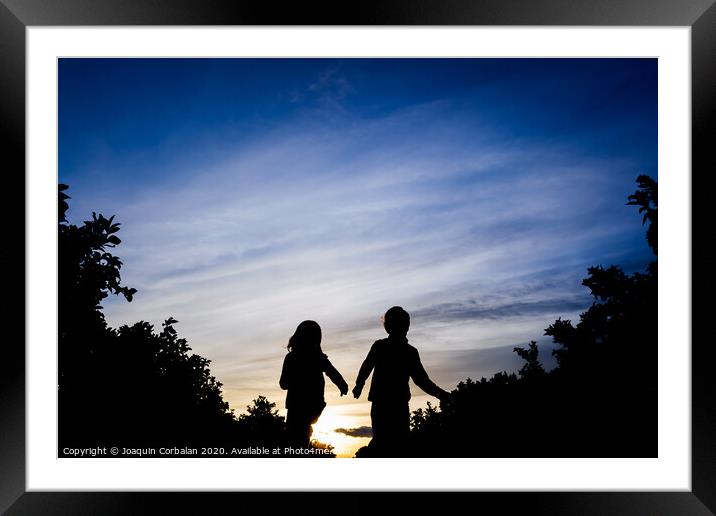 Silhouette of two children running through the field on a winter sunset. Framed Mounted Print by Joaquin Corbalan