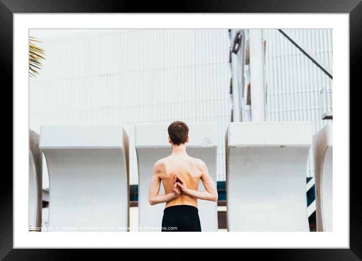 Young male athlete performing stretching exercises for back and arms in an urban place. Framed Mounted Print by Joaquin Corbalan