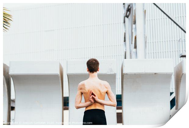 Young male athlete performing stretching exercises for back and arms in an urban place. Print by Joaquin Corbalan