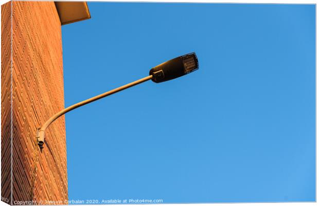 Lamppost on the red wall of a building, by day, with a blue sky background. Canvas Print by Joaquin Corbalan
