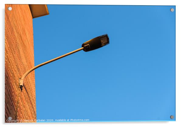 Lamppost on the red wall of a building, by day, with a blue sky background. Acrylic by Joaquin Corbalan