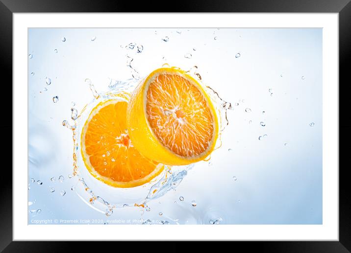 Two halves of orange fruit splashing into clear water. Framed Mounted Print by Przemek Iciak