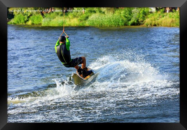 A wakeboarder rushes through the water at high speed along the green bank of the river. Framed Print by Sergii Petruk