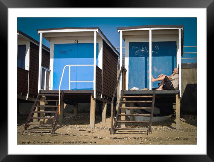 Beach huts at Thorpe Bay, Essex, with a person sitting on the floor talking on the phone. Framed Mounted Print by Peter Bolton