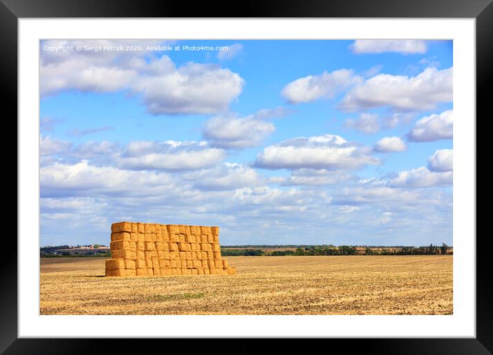 A large stack of straw against the background of a wide field and blue cloudy sky after harvest. Framed Mounted Print by Sergii Petruk