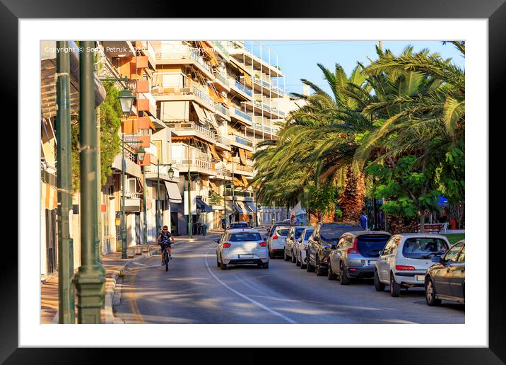 Street landscape of the summer city of Loutraki, Greece, with passing cars and a teenager on a bicycle. Framed Mounted Print by Sergii Petruk