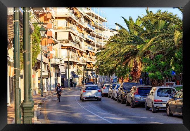 Street landscape of the summer city of Loutraki, Greece, with passing cars and a teenager on a bicycle. Framed Print by Sergii Petruk