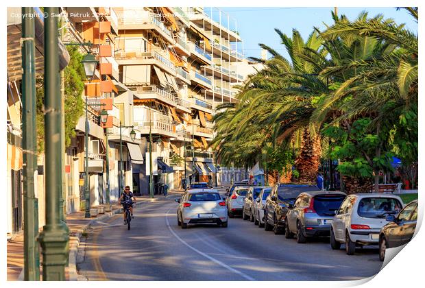 Street landscape of the summer city of Loutraki, Greece, with passing cars and a teenager on a bicycle. Print by Sergii Petruk