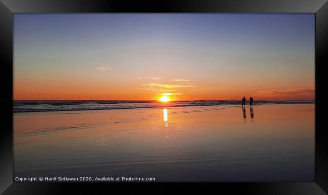 Silhouetted couple enjoys sunset at beach 1 Framed Print by Hanif Setiawan