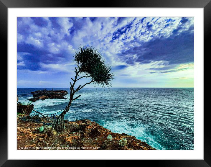 A palm tree and rock island in stormy sea Framed Mounted Print by Hanif Setiawan