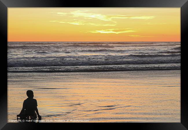 A young boy on wet sand beach at sunset. Framed Print by Hanif Setiawan