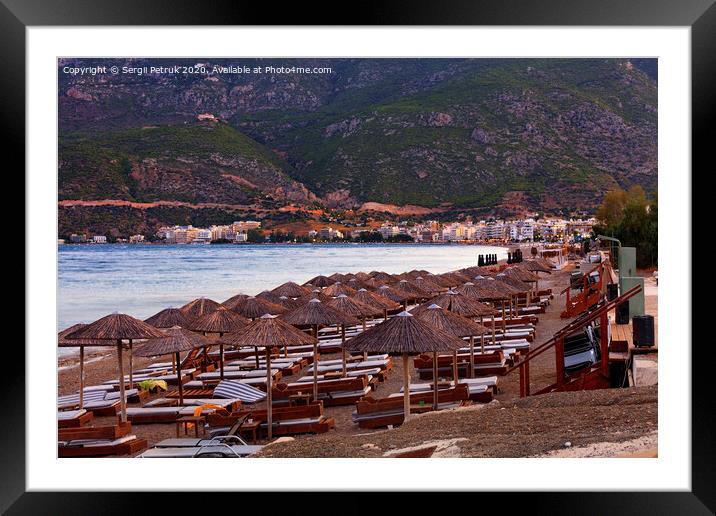 Thatched peaks of beach umbrellas and wooden deck chairs with mattresses on a deserted promenade among mountains and monasteries in the distance in the rays of the evening setting sun of the city. Framed Mounted Print by Sergii Petruk