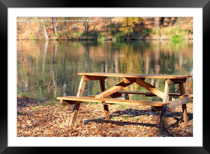 Wooden table with picnic benches in the open air on the background of fallen oak leaves near a forest lake. Framed Mounted Print by Sergii Petruk