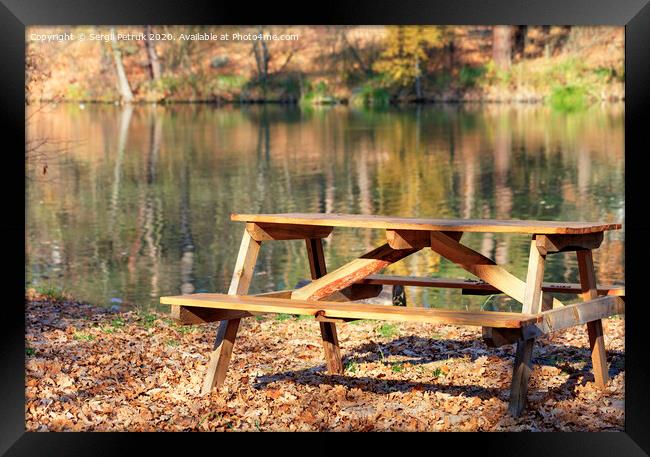 Wooden table with picnic benches in the open air on the background of fallen oak leaves near a forest lake. Framed Print by Sergii Petruk