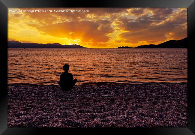 Silhouette of a teenager who sits on a pebble sea shore and watches a beautiful, vibrant sunset on the Gulf of Corinth in Greece. Framed Print by Sergii Petruk