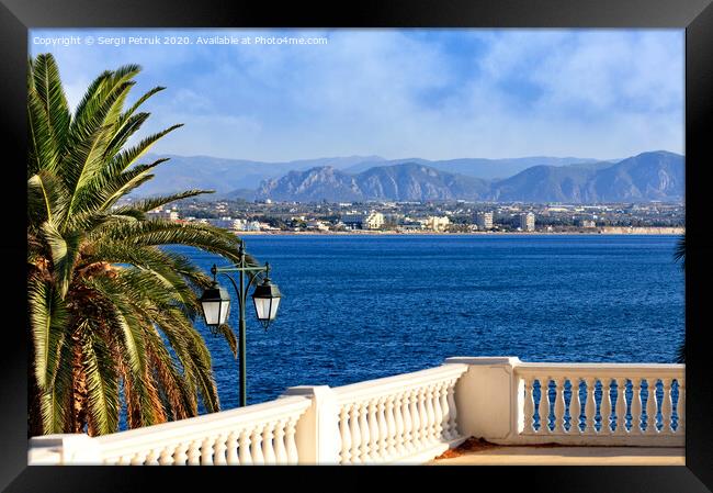 Beautiful seascape on the promenade, a street lamp under a palm tree looks at the sea, city and mountains in blur. Framed Print by Sergii Petruk