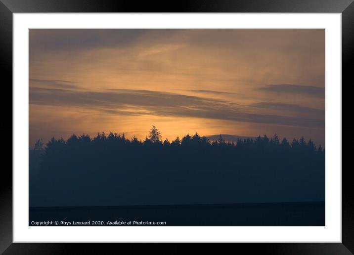 Amber glow at dusk, just after sunset, behind a coniferous forest Framed Mounted Print by Rhys Leonard