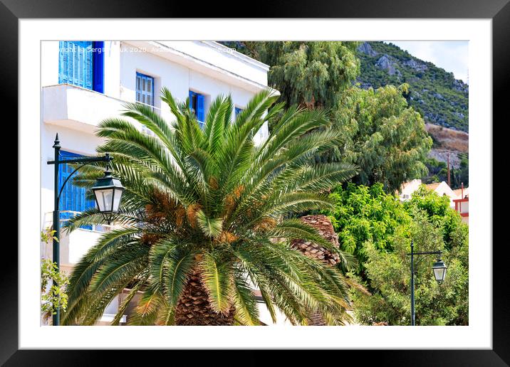 Beautiful landscape of a city street with growing date palm trees near a traditional white Greek house with blue wooden windows and doors. Framed Mounted Print by Sergii Petruk