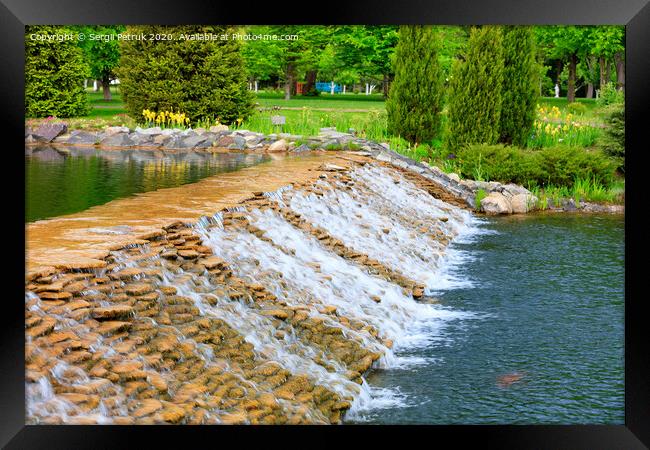 The waters of a beautiful decorative waterfall flow rapidly in a summer park. Framed Print by Sergii Petruk