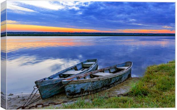 Two old blue-green boats moored by a metal chain to the shore of a calm river against the backdrop of the bright rising sun. Canvas Print by Sergii Petruk