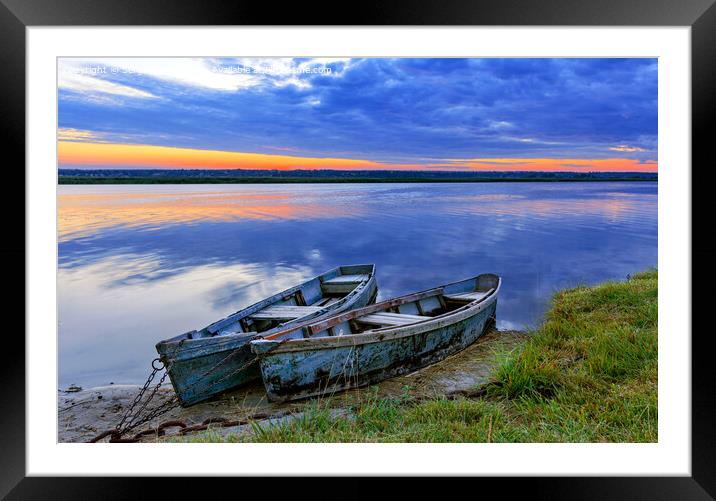 Two old blue-green boats moored by a metal chain to the shore of a calm river against the backdrop of the bright rising sun. Framed Mounted Print by Sergii Petruk