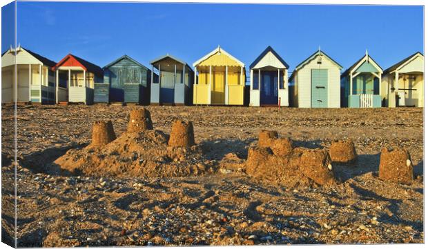 A row of beach huts at Thorpe Bay, Essex, UK, with sandcastles on the beach in the foreground. Canvas Print by Peter Bolton
