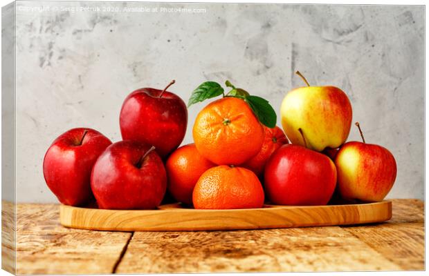 Red ripe apples and tangerines with green leaves lie on a wooden tray on an old wooden table with gray concrete background. Canvas Print by Sergii Petruk