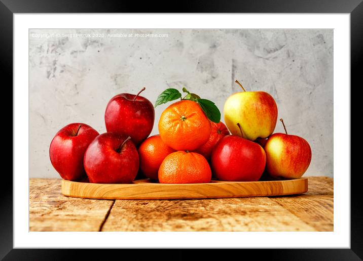 Red ripe apples and tangerines with green leaves lie on a wooden tray on an old wooden table with gray concrete background. Framed Mounted Print by Sergii Petruk