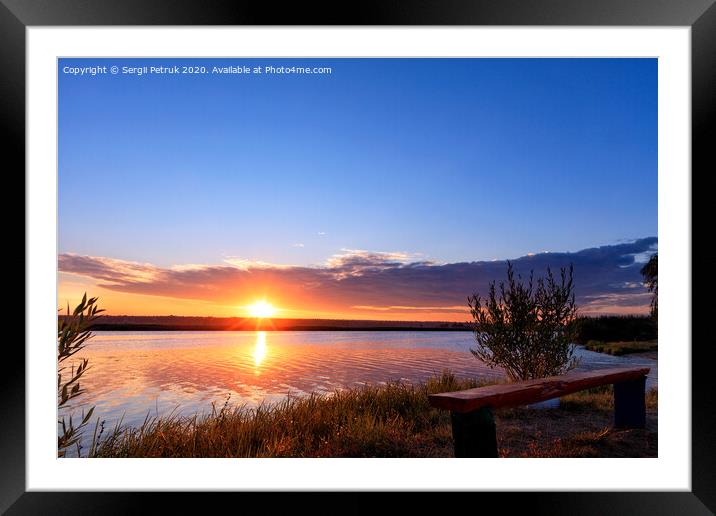 The bright rising sun rises above the horizon behind a wide river and is reflected in a wavy water surface. Framed Mounted Print by Sergii Petruk