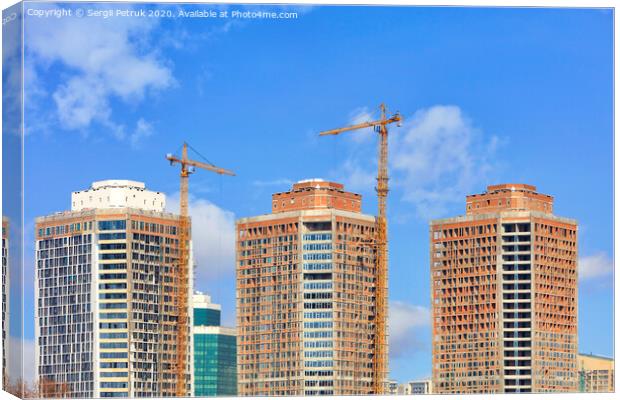 The construction of modern residential skyscrapers with a glass facade and tower cranes against the blue sky. Canvas Print by Sergii Petruk