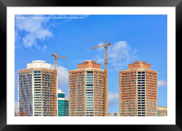The construction of modern residential skyscrapers with a glass facade and tower cranes against the blue sky. Framed Mounted Print by Sergii Petruk