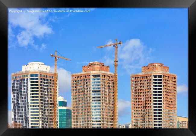 The construction of modern residential skyscrapers with a glass facade and tower cranes against the blue sky. Framed Print by Sergii Petruk