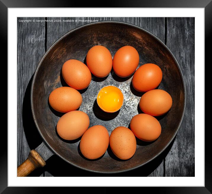 Brown chicken eggs in an old cast-iron frying pan look in the center at a broken egg with a bright yolk. Framed Mounted Print by Sergii Petruk