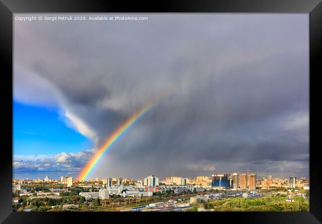 A bright rainbow in the sky above city houses after a thunderstorm separates thunderclouds from the clear sky. Framed Print by Sergii Petruk