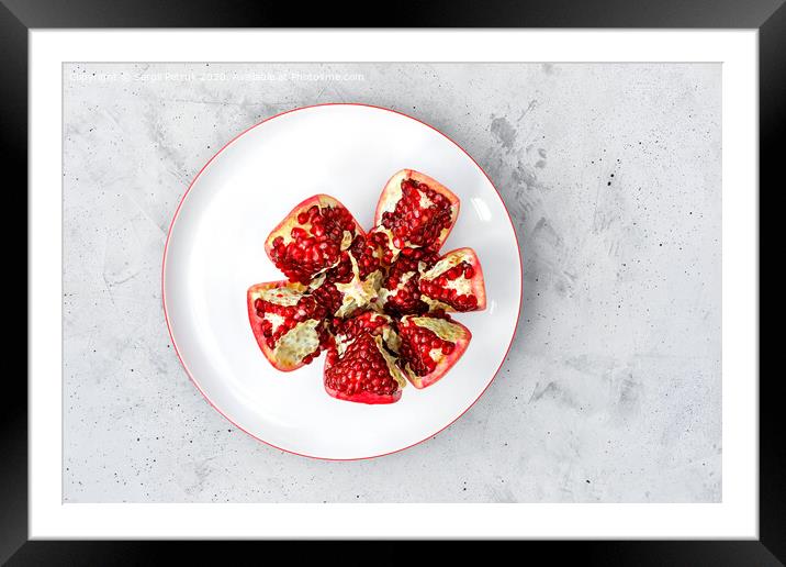 Ripe pomegranate is broken into segments and is on a white porcelain plate on a gray concrete background. Framed Mounted Print by Sergii Petruk