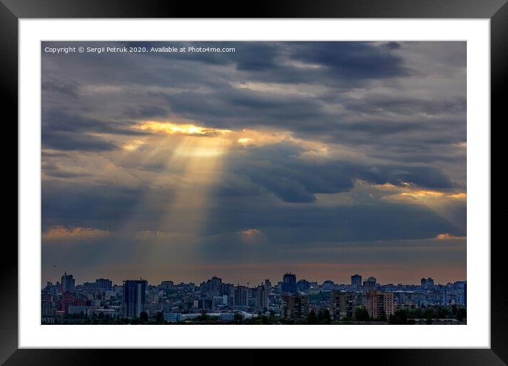 The sun's rays break through dense clouds at dawn over the city. Framed Mounted Print by Sergii Petruk