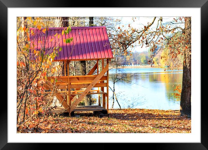 Wooden arbor with a table and picnic benches in the open air on the background of fallen leaves near a forest lake. Framed Mounted Print by Sergii Petruk