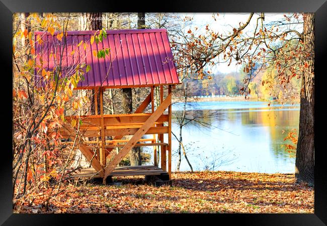 Wooden arbor with a table and picnic benches in the open air on the background of fallen leaves near a forest lake. Framed Print by Sergii Petruk