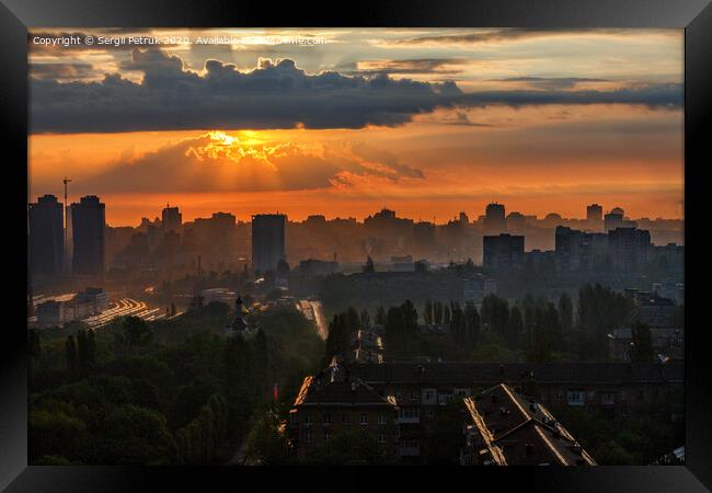 The sun's rays break through the rain clouds of a cloud at dawn and illuminate a sleeping city. Framed Print by Sergii Petruk