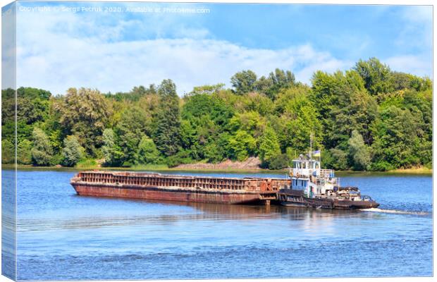 A river tug is pushing a rusty barge along the river along the shore. Canvas Print by Sergii Petruk