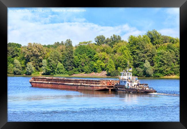 A river tug is pushing a rusty barge along the river along the shore. Framed Print by Sergii Petruk